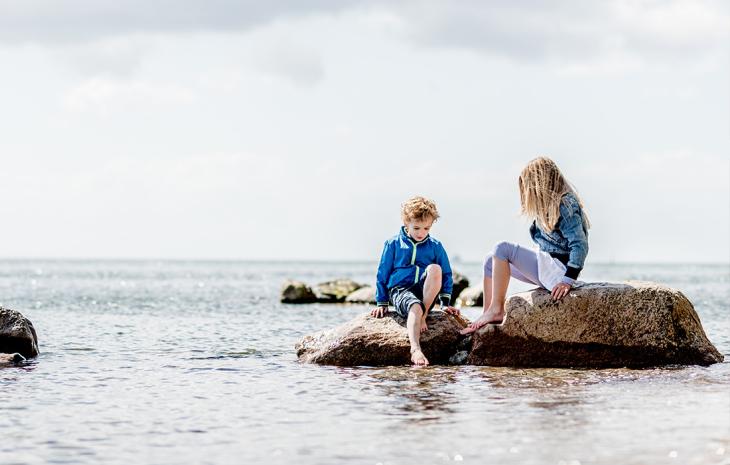 På sten i vandkanten sidder to børn